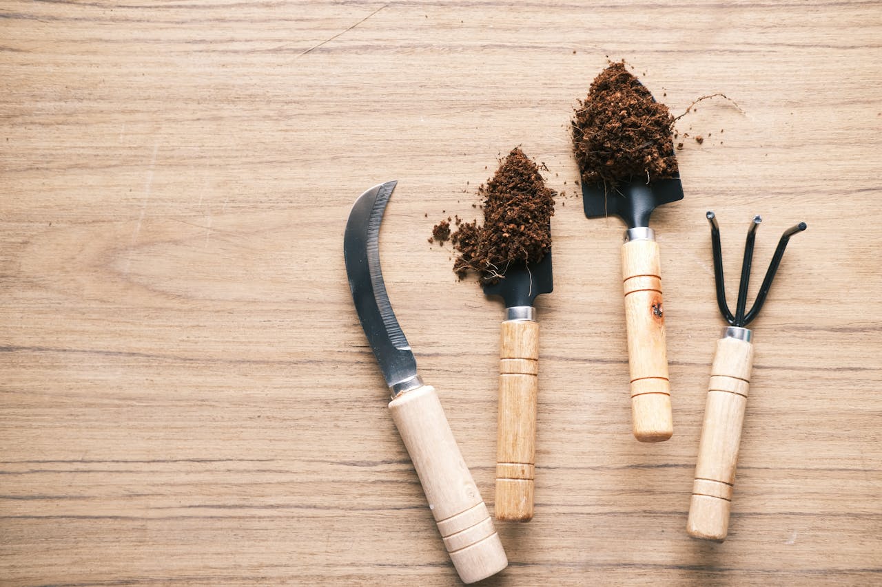 Flat lay of gardening tools on wooden table accompanied by soil.