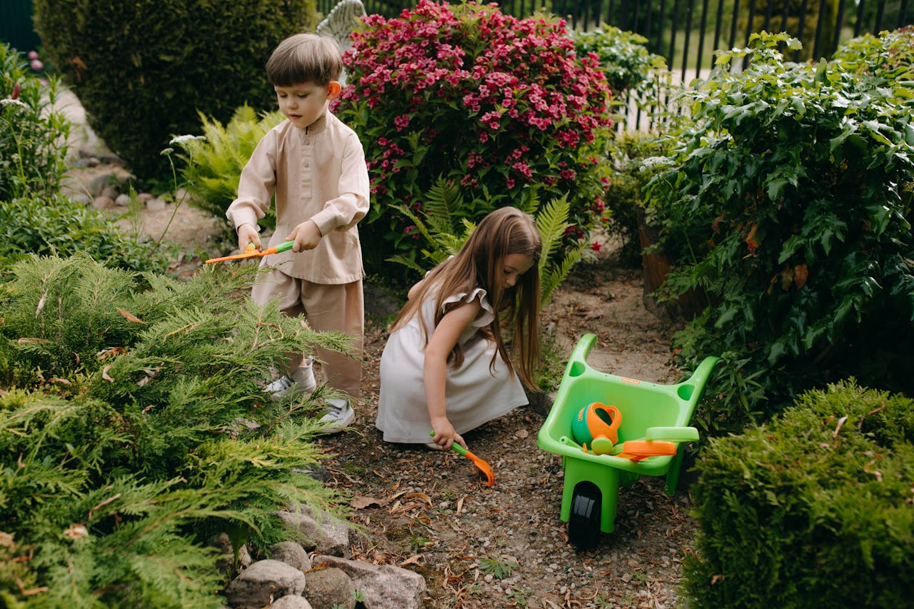 Two children engage in gardening activities with tools in a vibrant summer garden, fostering creativity and play.